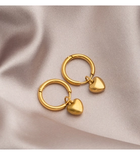 Detailed view of gold heart dangle hoop earrings on elegant champagne satin fabric