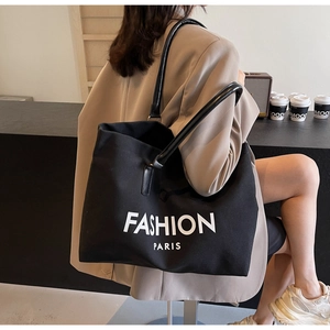 Detail of black canvas tote bag with leather straps and Fashion Paris logo on a shoulder