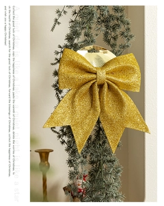 Detail of a sparkling gold glitter Christmas bow ornament hanging on a pine tree branch