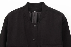 Detail der schwarzen Baseballjacke mit geripptem Kragen, Pattentaschen und mattem Knopf