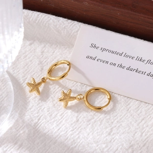 Golden starfish pendant hoop earrings with textured finish on white fabric
