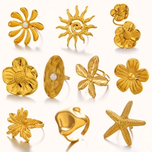Set aus goldenen Edelstahlringen mit Blumen-, Sonnen- und Perlendesign auf warmem Weiß