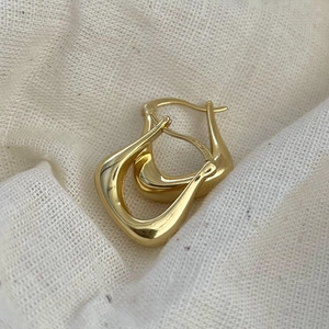 Irregular U-shape 925 sterling silver earrings in gold finish on white linen background