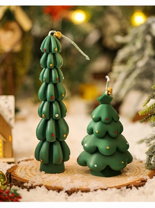 Mini green Christmas tree candles with colorful dots and gold bells on snowy wood base