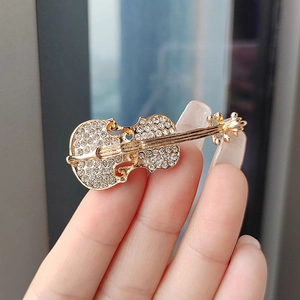 Close-up of elegant gold violin brooch with rhinestones held in hand against sunlight