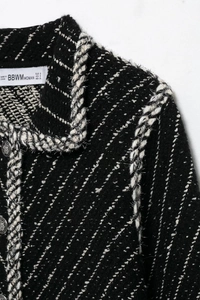 Detailed macro view of black tweed jacket with silver woven trim and metallic button