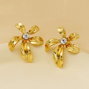Macro shot of gold floral earrings with a central white zircon on a beige pedestal
