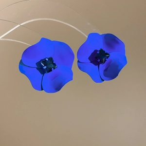 Detailed shot of blue matte floral earrings with square dark crystal centers on beige background