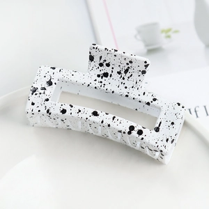 Detail of white square hair claw clip with black ink splatter pattern on a white plate