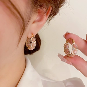 Detail of gold hoop earring with pink cat-eye stone and sparkling rhinestones
