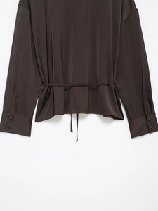 Detail of dark brown satin shirt featuring a cinched waist with ties and buttoned cuffs