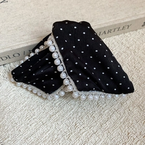 Detail of polka dot satin hair claw clip with white faux pearl trim on fabric background
