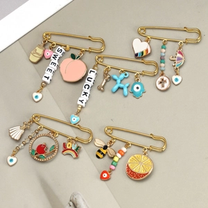Detailed view of gold safety pins with colorful enamel fruit and evil eye charms