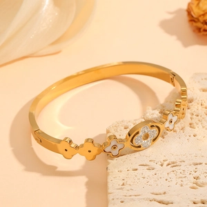 Golden stainless steel bangle with white clover shells and subtle crystal accents