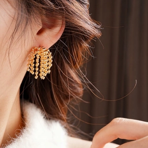 Golden beaded tassel earrings featuring a fan-shaped fringe design on a model