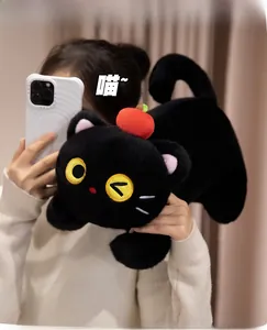 Close-up of black plush cat toy with red apple on head and cute winking yellow eyes