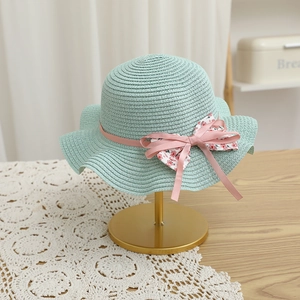 Détail du chapeau de paille vert menthe avec ruban rose, noeud floral et bord festonné