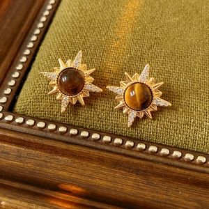 Close-up of gold starburst earrings with brown tiger eye stone and crystals