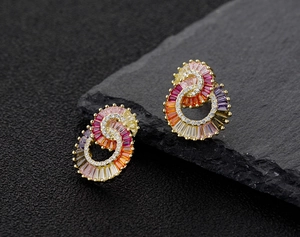 Macro detail of geometric gold earrings with multicolored zircon stones on stone background