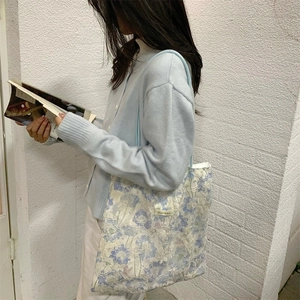 Detail of floral lace embroidery on a light blue tote bag carried by a model