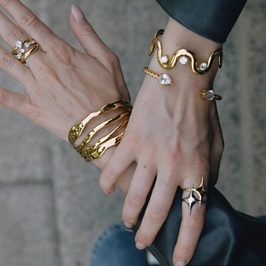 Outdoor natural light shot of layered gold wave bracelets and zircon drop rings on a model