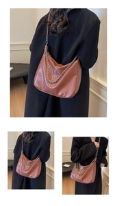 Detail of brown leather hobo bag featuring white stitching and silver metal chain strap