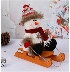 Close-up of a plush Christmas snowman doll sitting on a wooden sled with cozy knit details