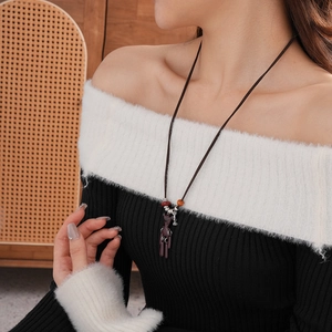 Detailed close-up of brown cord sweater necklace with metal bear pendant and red beads