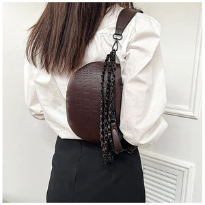 Detail of dark brown crocodile-patterned chest bag with chunky black chain decoration