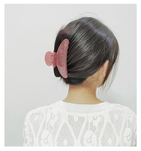 Detailed close-up of a pink glitter acrylic shark hair claw clip worn by a model