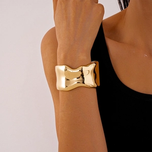 Close-up of golden irregular wavy cuff bracelet showing glossy metallic texture and wide design
