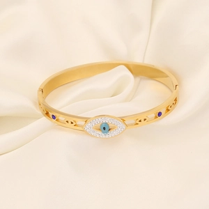 Detailansicht eines goldenen Evil-Eye-Armreifs mit blauen Edelsteinen auf Seide