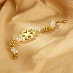 Macro detail of gold clover bracelet with pearls on a luxury satin background