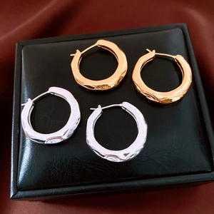 Detailed close-up of gold and silver irregular textured hoop earrings on a black box