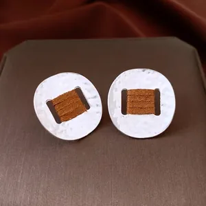 Oval hammered metal stud earrings with dark brown suede wrap on textured display