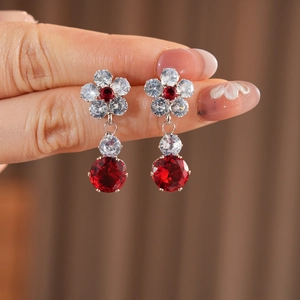 Detailed macro view of red zircon flower earrings held by hand showing delicate craftsmanship