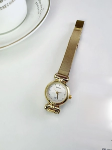 Detail of BARSH gold mesh watch with white dial and crystal markers on a magazine