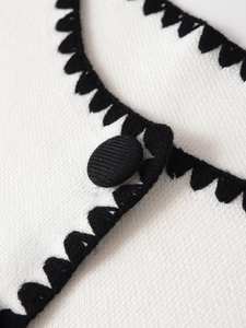Detailansicht der Strickstruktur mit schwarzen Kontrastkanten und Stoffknöpfen am Oberteil