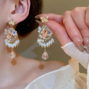 Close-up of champagne pink teardrop gemstone earrings with bow and floral accents