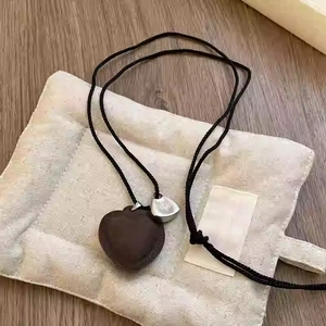 Detail of heart pendant with black braided rope and silver tag on a beige bag