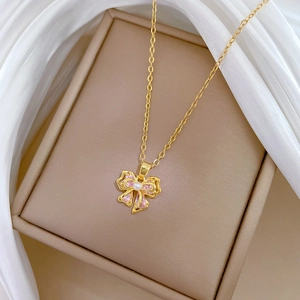Detail of gold bow necklace featuring pink gemstones and a pearl on a silk background