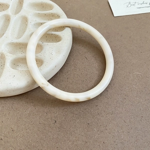 Macro detail of minimalist cream resin bangle with brown marble texture on ceramic tray