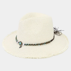 Detailed macro view of beige straw hat featuring turquoise beads and metal leaf charm