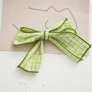 Detail of light green plaid fabric bow hair clip with dark green edges on card