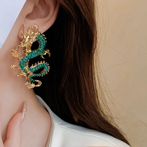 Primo piano di un ear cuff a forma di drago dorato con zirconi verdi sull'orecchio della modella