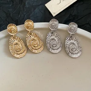 Elegant gold and silver oval drop earrings with spiral texture on a white plate