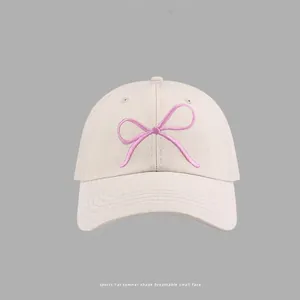 Detailed shot of pink bow embroidery on a beige cotton baseball cap with neat stitching