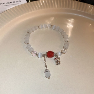 Detail of beaded bracelet featuring a silver bear charm and white cat eye stones