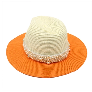 Detail of hand-woven straw hat brim with elegant pearls and vibrant orange contrast