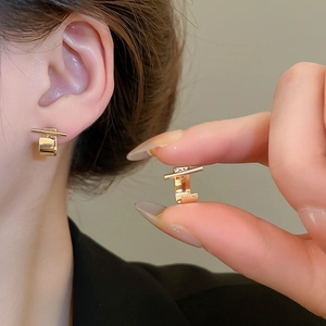 Close-up of minimalist gold geometric stud earrings worn on ear with polished metal shine